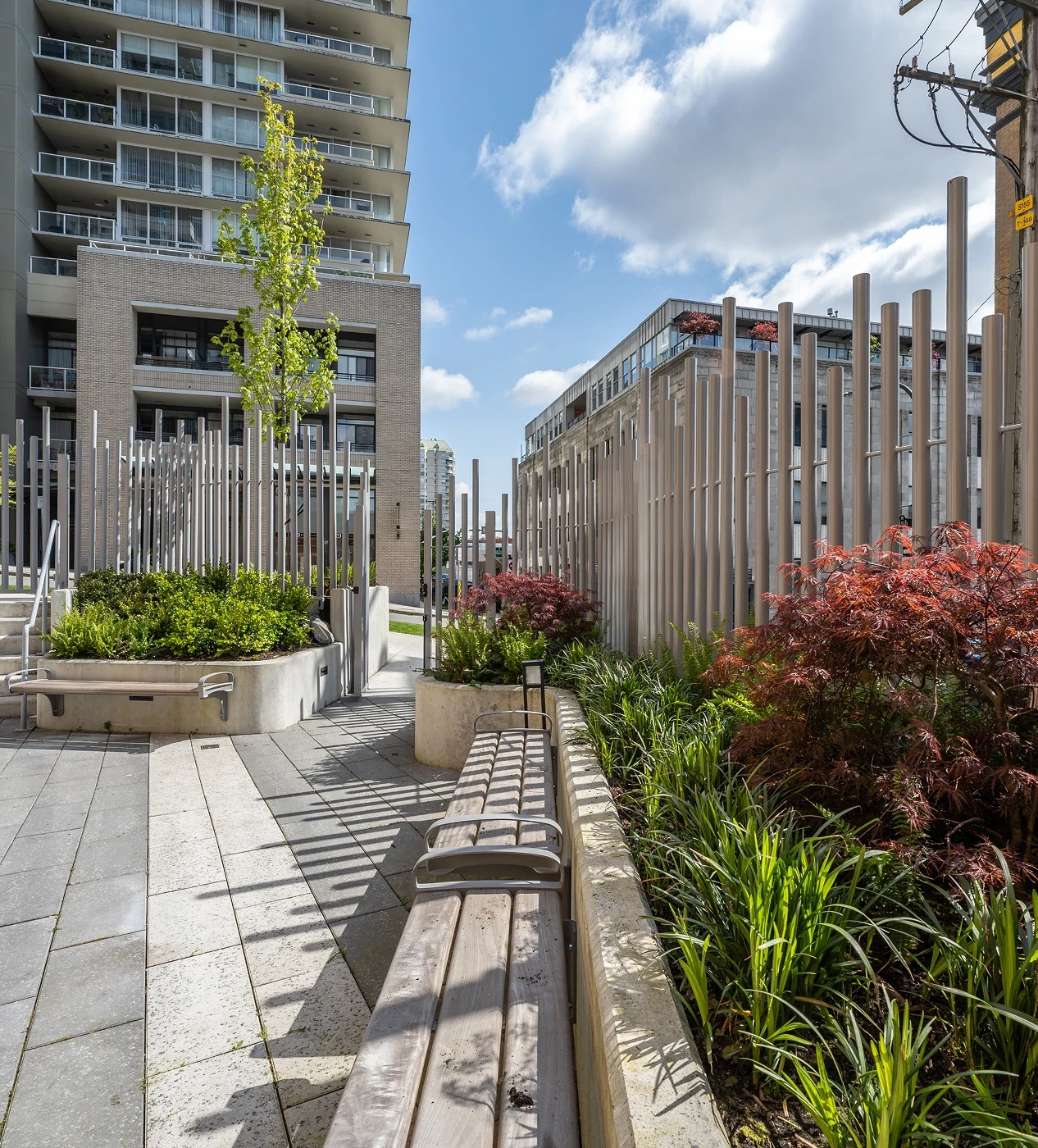Planted walkway with timber benches and vertical posts between towers